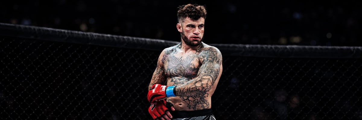 Tattooed male fighter flexing at weigh-ins wearing shorts with blue and white trim