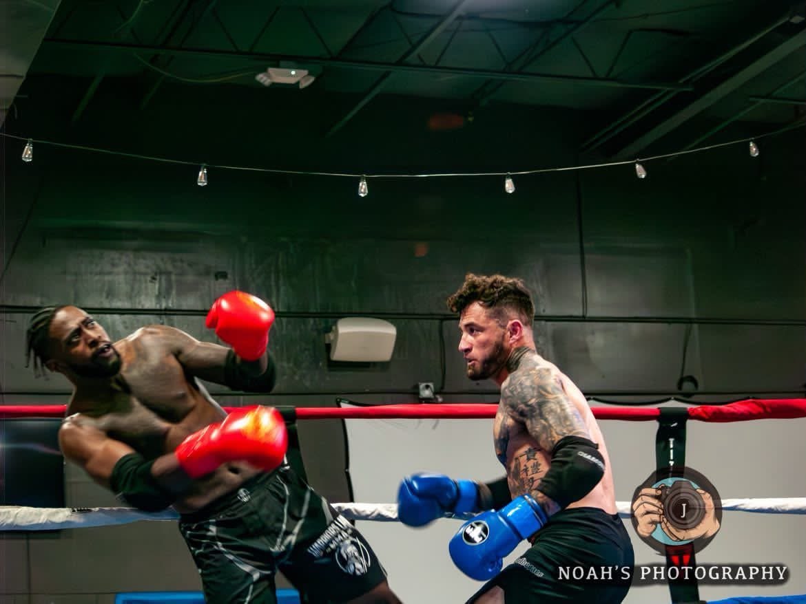Two male boxers sparring in a boxing ring, one throwing a punch while the other defends with red gloves